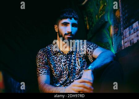 Porträt eines jungen bärtigen Mannes, der an der beleuchteten Bar sitzt Stockfoto
