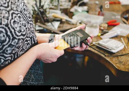 Mittelteil der älteren Frau mit Kreditkarte Leser in Schmuck Werkstatt Stockfoto