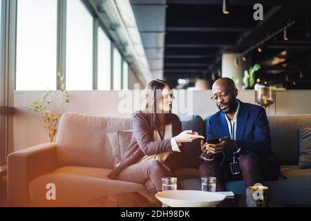 Geschäftsmann, der Geschäftsfrau Smartphone zeigt, während sie im Büro sitzt Stockfoto