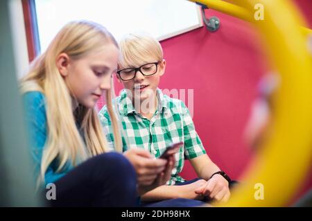 Junge mit Freundin, die das Handy über die Treppe benutzt Schule Stockfoto