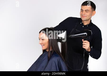 Ein professioneller männlicher Friseur trocknet die Haare einer jungen Frau mit einem bafu. Geschlechterstereotypen. Weißer Hintergrund. Stockfoto