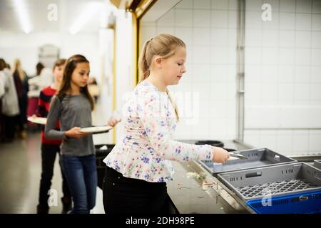 Mädchen Putting Teller in Kiste nach dem Mittagessen in der Schule Cafeteria Stockfoto