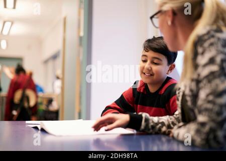 Mittelerwachsener Lehrer unterrichtet Jungen am Schreibtisch im Klassenzimmer Stockfoto