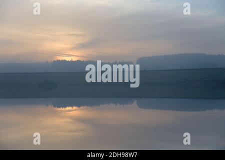 Der goldene Sonnenuntergang, der von Nebel und Wolken verdeckt wird, ist ein Rückfall auf 12 entfernte Figuren, die entlang der Redmires-Stauseen-Staumauer spazieren. Kalter Tag am Ende des Herbstes. Stockfoto