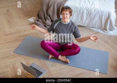 Eine ältere Frau praktiziert Yoga. Ein Heimtraining unter Anleitung eines Online-Trainers. Nahaufnahme. Stockfoto