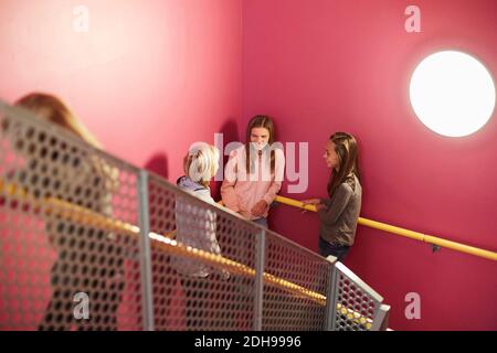 Lächelndes Mädchen im Gespräch mit Freunden gegen rosa Wand in der Mitte Schule Stockfoto