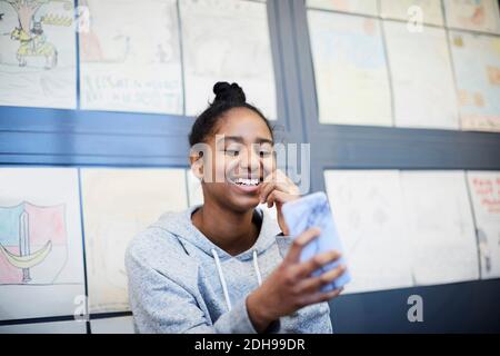 Lächelndes Mittelschulmädchen mit Handy gegen Zeichnungen in Korridor Stockfoto