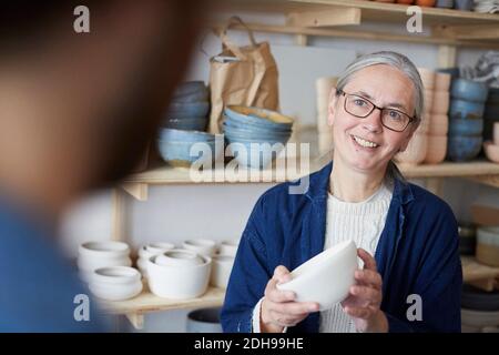 Lächelnde reife Frau diskutieren mit Mann über Schüssel in Keramik Klasse Stockfoto