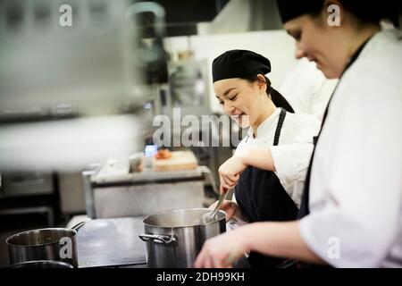Weibliche Chefstudentin mit Kollegen, die Essen in der kommerziellen Küche kochen Stockfoto