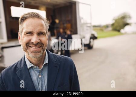 Portrait von glücklichen Geschäftsmann stehen auf der Straße mit Kollegen und Tragbarer Bürowagen im Hintergrund Stockfoto