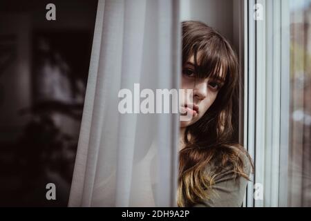 Portrait der Frau durch Fenstervorhang Stockfoto