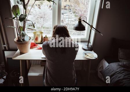 Rückansicht einer besorgten Frau, die am Fenster saß Stockfoto