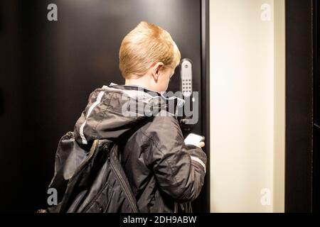 Rückansicht des Jungen mit App auf Smartphone zu Entriegeln Sie die Tür Stockfoto