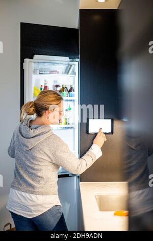 Frau, die ein digitales Tablet auf einem intelligenten Kühlschrank im modernen Zuhause verwendet Stockfoto