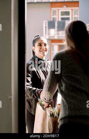 Junge Liefererin, die Lebensmittel an weibliche Kundin zu Hause liefert Stockfoto