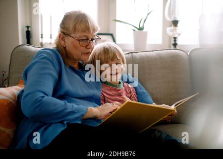 Großmutter liest das Storybook für Enkel, während sie auf dem Sofa sitzt Wohnzimmer Stockfoto