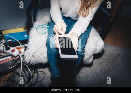 Mittelteil der Frau stecken in Handy-Laden im Studentenwohnheim Zimmer Stockfoto