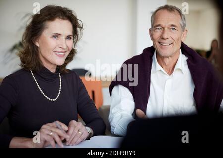 Lächelnde ältere Frau, die mit dem Mann während des Treffens beim Gesetz sitzt Fest Stockfoto