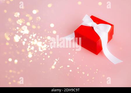 Rote Geschenkbox mit weißem Band, glitzernden Bokeh-Leuchten in Gold und rosa Hintergrund Stockfoto