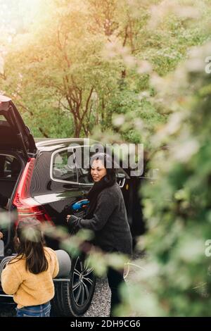 Mutter lädt Elektroauto, während Tochter Gepäck lädt Stockfoto