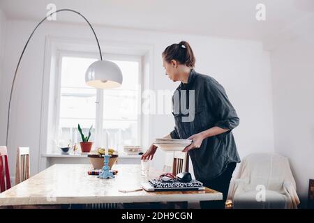 Seitenansicht der Frau, die Teller auf dem Esstisch anordnete Zu Hause Stockfoto