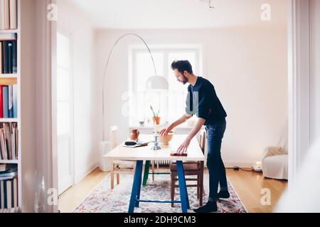 Seitenansicht des Mannes, der zu Hause einen Esstisch arrangiert Stockfoto