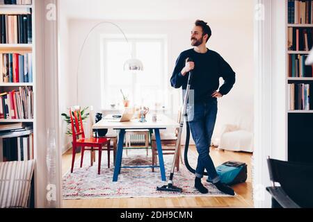 Glücklicher Mann, der mit dem Staubsauger im Speisesaal stand Zu Hause Stockfoto