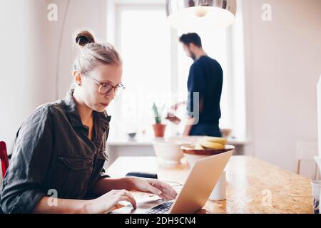 Frau arbeitet auf Laptop gegen Mann Gießanlage zu Hause Stockfoto