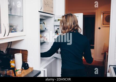 Rückansicht der Frau, die den Kühlschrank in der Küche zu Hause öffnet Stockfoto