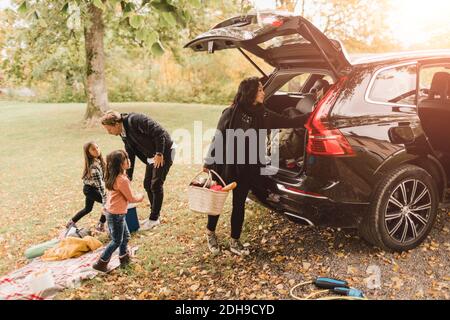 Familie Entladen Gepäck aus dem Elektroauto auf dem Feld während des Picknicks Stockfoto