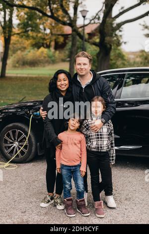 Porträt von Vater und Mutter stehen mit Töchtern gegen elektrische Auto Stockfoto