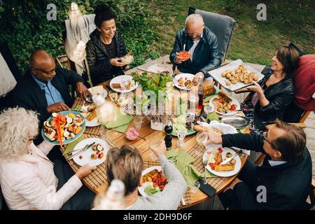 High-Angle-Ansicht von älteren männlichen und weiblichen Freunden genießen Abendessen am Esstisch während der Gartenparty im Garten Stockfoto