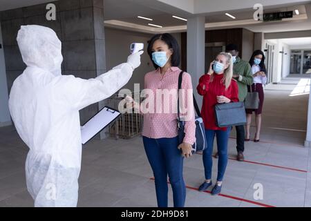 Gesundheitsarbeiter trägt Schutzkleidung Überprüfung der Temperatur der Geschäftsfrau Stockfoto