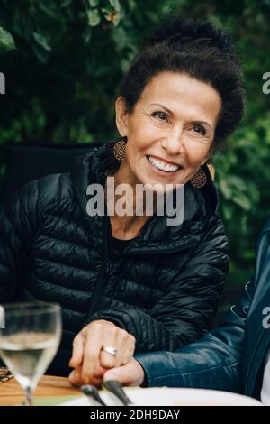 Lächelnde ältere Frau, die die Hände des Mannes hält, während sie ansitzt Esstisch während Gartenparty Stockfoto