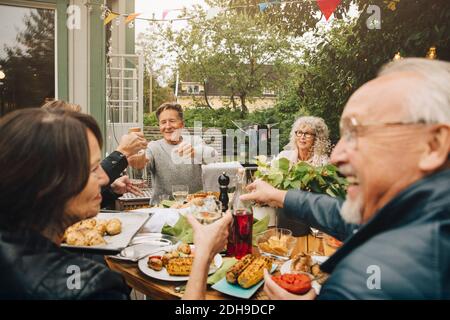 Glückliche ältere männliche und weibliche Freunde genießen Abendessen Party während Sitzen am Esstisch im Hinterhof Stockfoto