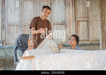 Ein Mann, der beiden Frauen beibringt, wie man das Canting benutzt Für die Draw Batik Stockfoto