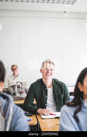Lächelnder junger Mann, der im Klassenzimmer am Schreibtisch sitzt Stockfoto