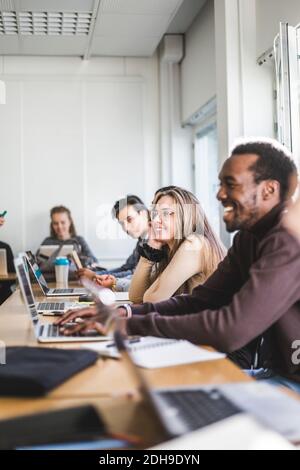 Lächelnde junge Frau, die im Klassenzimmer der Universität am Schreibtisch sitzt Stockfoto