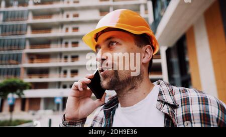 Porträt eines jungen Handwerkers, der beim Stehen auf der Baustelle anruft. Techniker, der auf einer Baustelle telefoniert Stockfoto