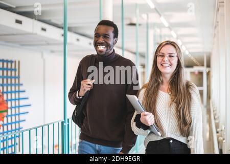Lächelnde männliche und weibliche Studenten, die im Korridor der Universität spazieren Stockfoto