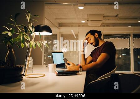 Erschöpfter Geschäftsmann mit Kopf in der Hand, der spät bei Creative arbeitet Büro Stockfoto