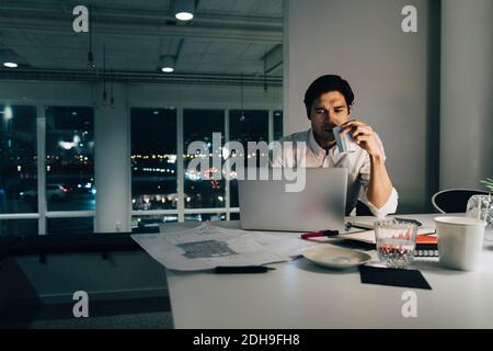 Engagierter Geschäftsmann hält Kaffeetasse, während er spät im Büro arbeitet Stockfoto