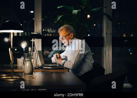 Engagierter männlicher Senior-Profi, der spät am kreativen Arbeitsplatz arbeitet Stockfoto