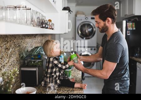 Seitenansicht des Vaters, der dem Mädchen auf dem Platz eine Flasche gab Theke in der Küche Stockfoto