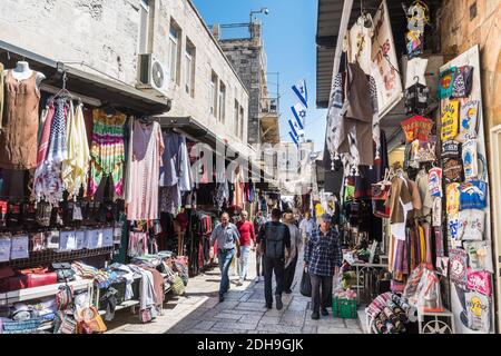 Blick auf die Straße mit vielen Touristen zu Fuß auf den Märkten in der Altstadt von Jerusalem am Tempelberg mit Hintergrund der israelischen Nationalflaggen. Stockfoto