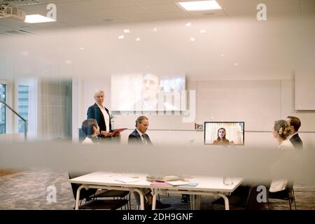Männliche und weibliche Führungskräfte diskutieren in Web-Konferenz Sitzung gesehen Durch Glas am Arbeitsplatz Stockfoto