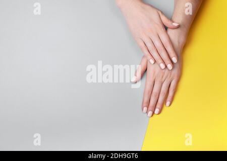 Schöne weibliche Hände mit einer klassischen matten Maniküre auf einem grau-gelben Hintergrund. Ort für Ihren Text. Stockfoto