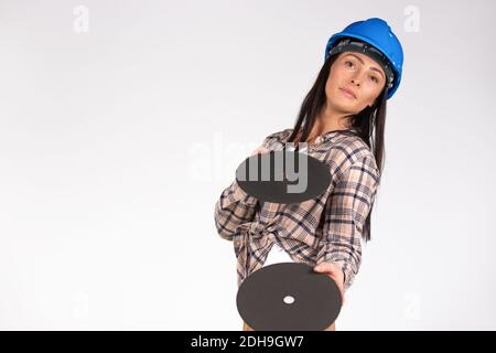 Eine Frau in einem blauen Harthut posiert auf einem weißen Hintergrund mit Schleifscheiben. Seitenraum. Stockfoto