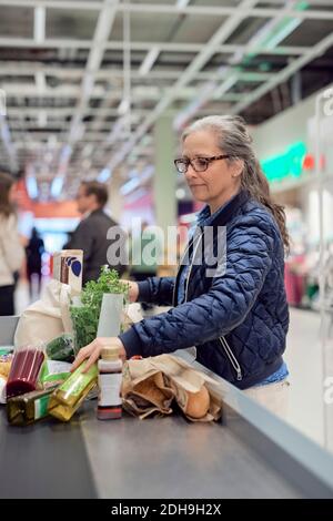 Ältere Frau steht mit Lebensmitteln und Tasche an der Kasse Im Supermarkt Stockfoto