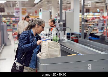 Lächelnde reife Frau hält Tasche an der Kasse im Supermarkt Stockfoto